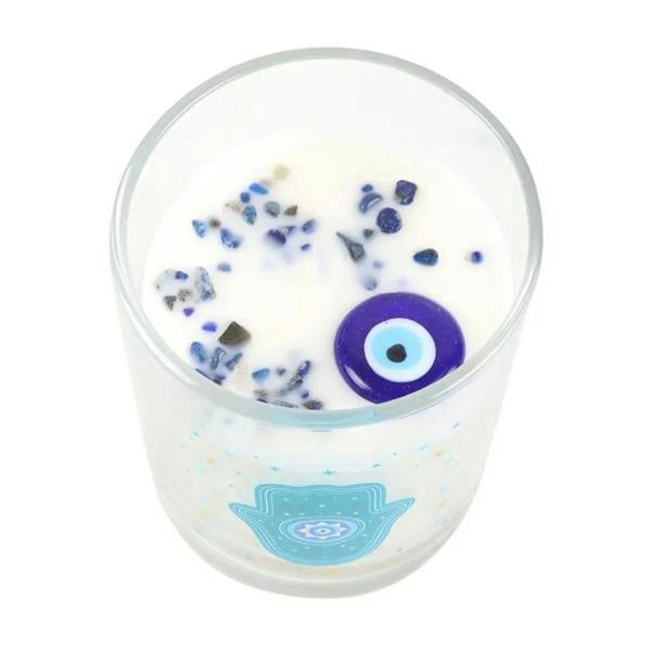 Clear glass candle with creamy wax, blue rock-like pieces, and a purple evil-eye charm