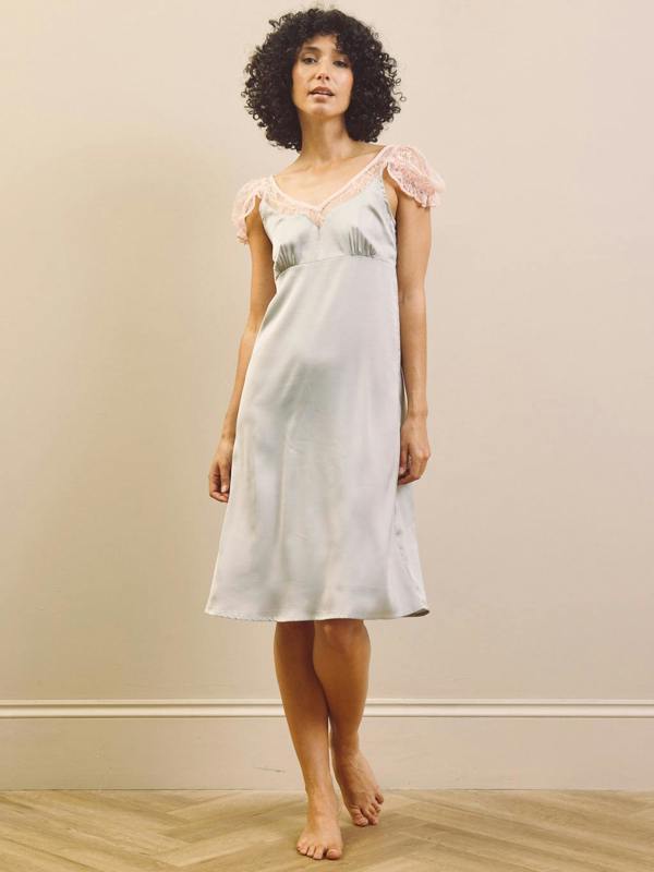 Woman wearing a light blue slip nightdress with lace trim against a beige wall.