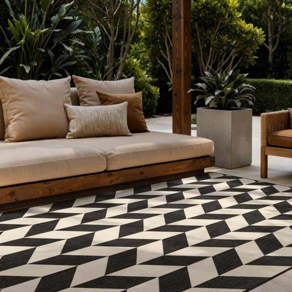 Outdoor seating area with a geometric patterned rug, cushions, and plants.
