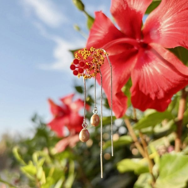 Silver threader earrings with pink pearls, displayed against a vibrant red hibiscus.