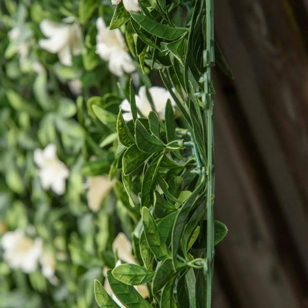 Close-up of artificial hedge panel edge with green leaves and white rhododendron blooms