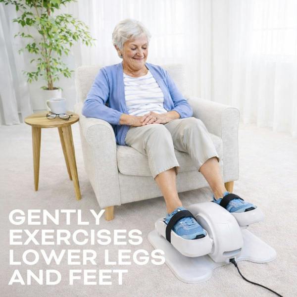 An older woman sits on a white armchair, smiling and relaxed as she uses the Reviber Motorised Mini Elliptical Bike by Reviber for low-impact leg exercise. Text reads: Gently exercises lower legs and feet.