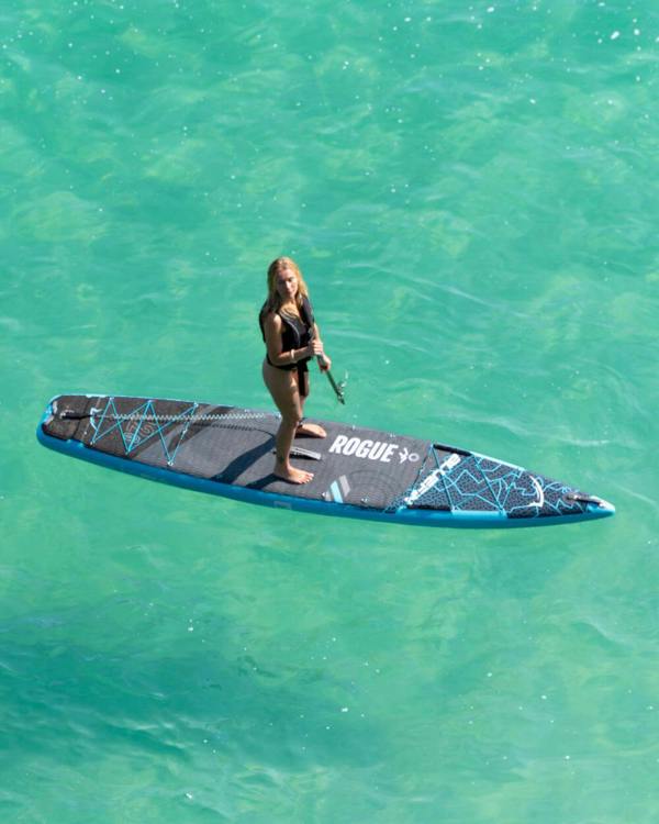 Paddleboarder on a turquoise sea, holding a paddle on a Rogue SUP. Ideal for water sports enthusiasts.