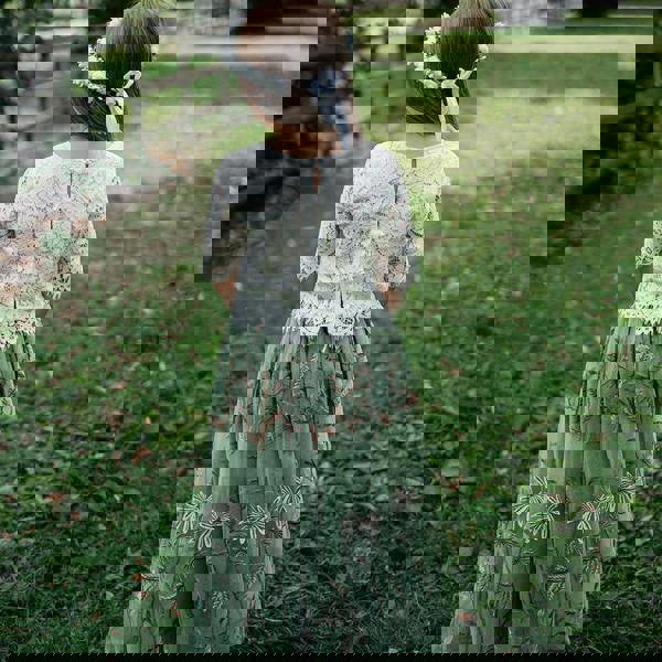 Child in a green dress with floral embroidery standing in a grassy field.