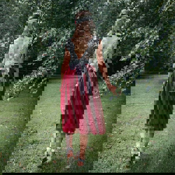 Girl in a red dress with a white lace top walking outdoors on grass.