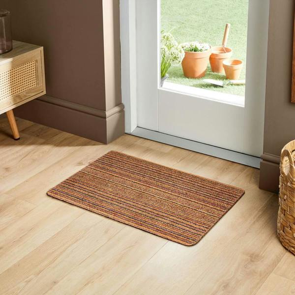 Doormat on a wooden floor with a glass door and potted plants in the background