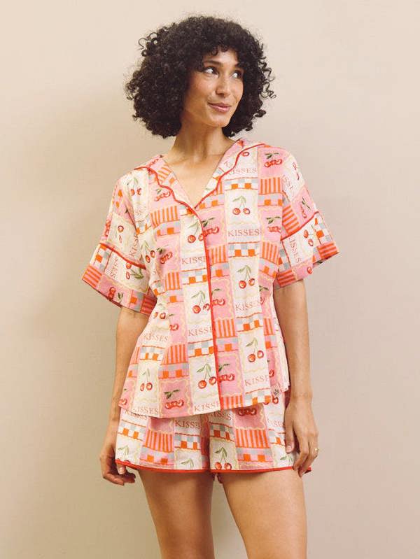 Woman wearing a cherry patterned pyjama set against a plain background