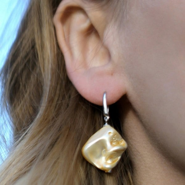 Golden shell earrings by LENAE London shown on a ear.