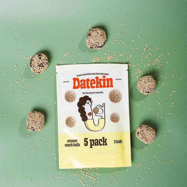 Datekin sesame snack balls packaging with scattered snack balls on a green background