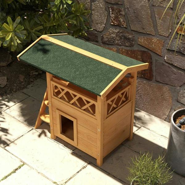 Outdoor wooden cat house angled view with green felt roof, balcony railings, and square door