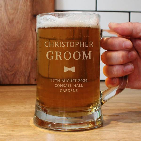 A close-up of a person holding a large glass tankard filled with beer, custom engraved with the name Christopher and the role Groom.