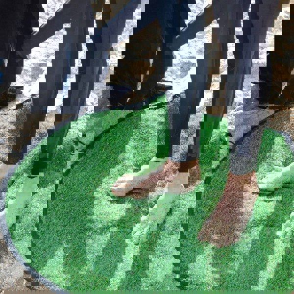 Person wearing a wetsuit standing on a green mat in the sand