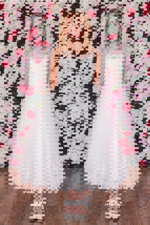 Young girl in a white dress standing against a floral wall.