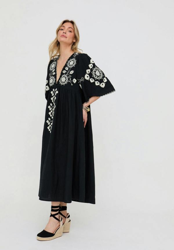 Woman wearing a black dress with white embroidery on a white background