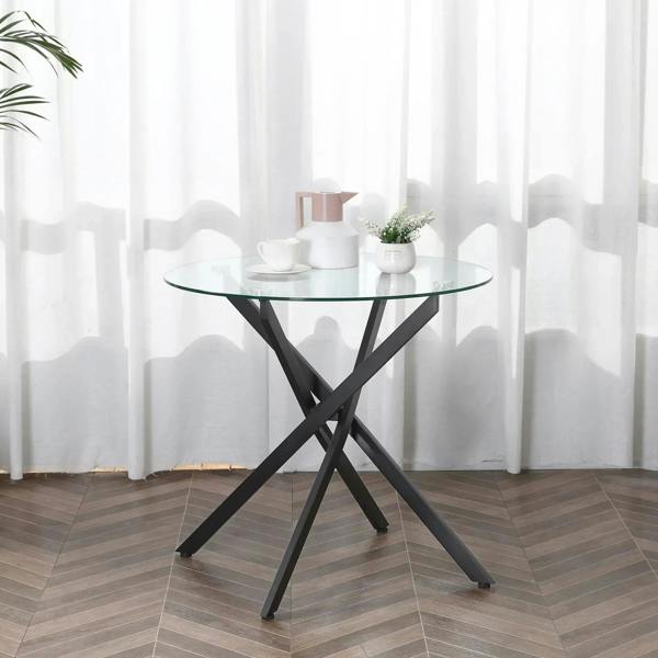 Round clear glass dining table with black crossed metal legs and minimal modern design