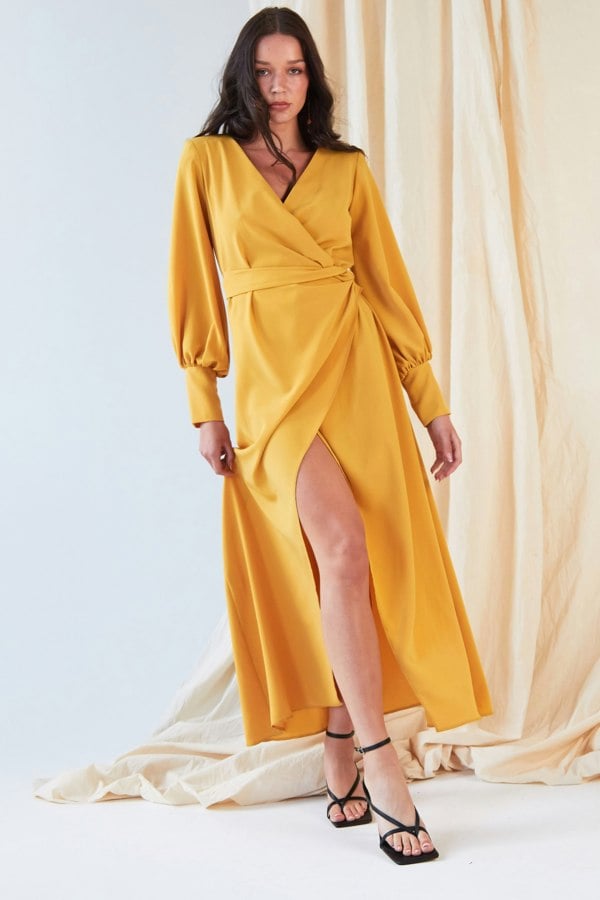 The model is wearing a Sarvin Mustard Wrap Dress with slits.