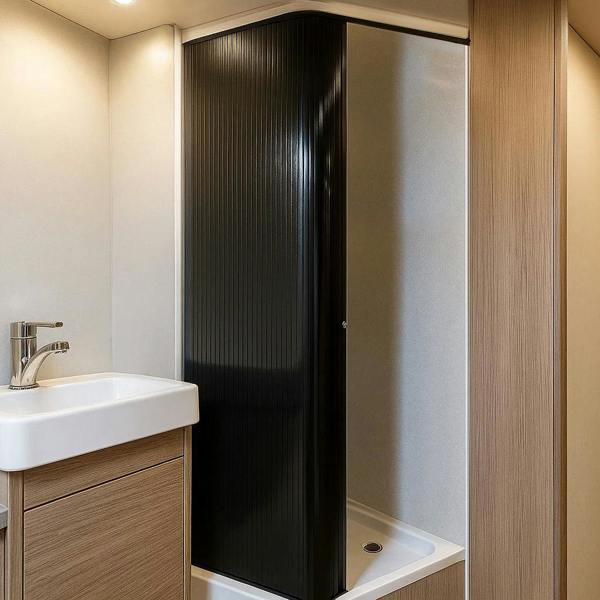 Sleek black Tambour shower door with vertical ribbing, framed in a modern bathroom setting with light wood accents and a white sink