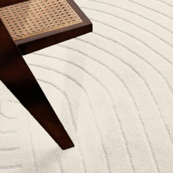 Close-up of a textured white rug with a dark wooden stool corner.