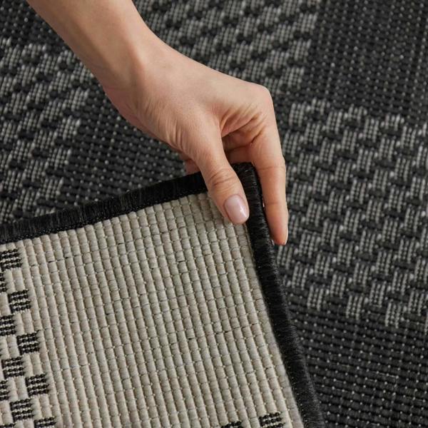 Hand holding a corner of a black and gray textured rug
