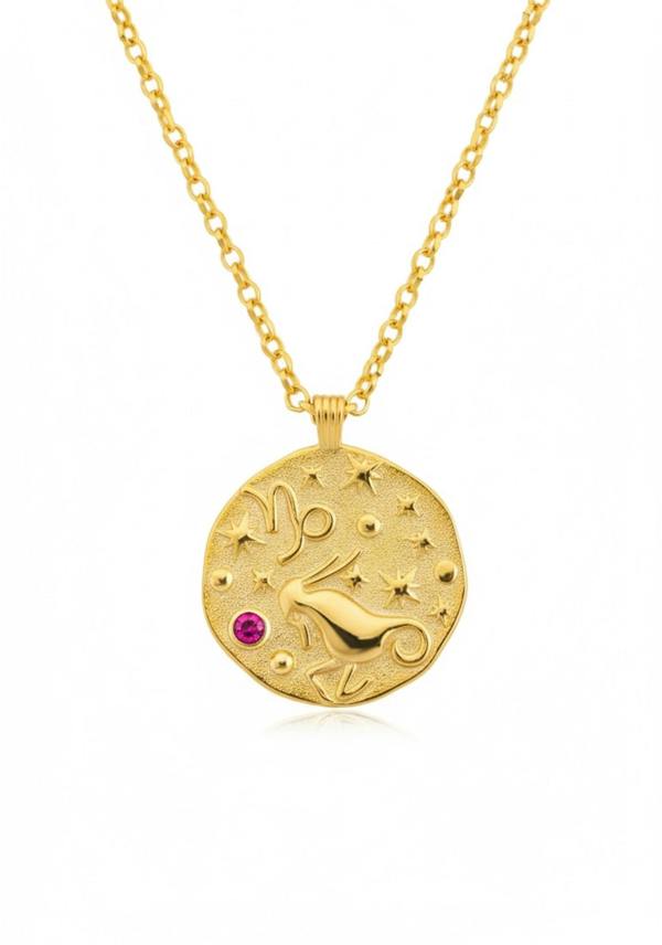 Gold necklace with a circular pendant featuring a design and a red gemstone on a white background