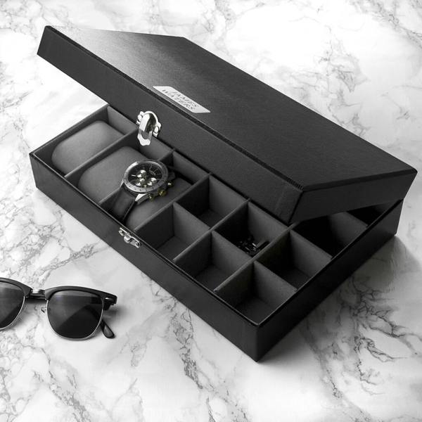 An open black mock-croc PU leather watch and cufflinks box with a grey suede interior containing a watch, sitting next to sunglasses on a marble surface.