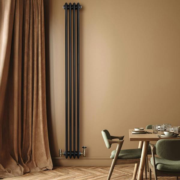 Traditional black 4 column radiator with valves, mounted on a beige wall, complementing a stylish dining area with wooden flooring