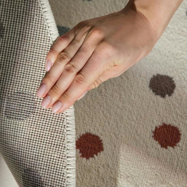 Hand touching a textured fabric surface with a pattern of brown dots.