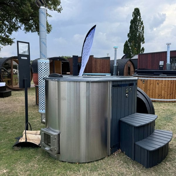 A wood-fired ofuro style hot tub with integrated heater, featuring a fibreglass liner and surrounded by wooden steps, a chimney guard, and a drinks shelf.