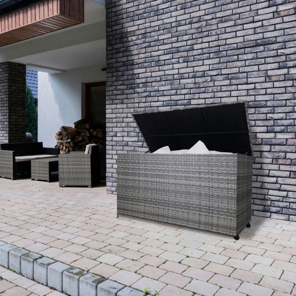Grey rattan storage box with a spacious interior, textured weave, and a hinged lid, placed on a patio against a brick wall