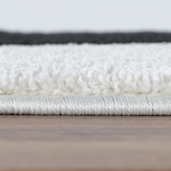 Close-up of a textured white rug on a wooden floor with a light gray background