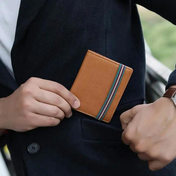 Person holding a cognac leather wallet with striped band against a blurred outdoor background