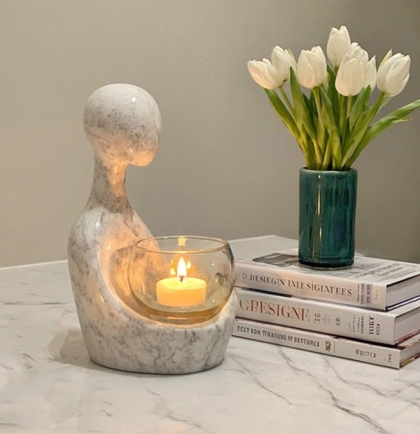 Decorative candle holder with a lit candle, vase of white tulips, and books on a marble surface.