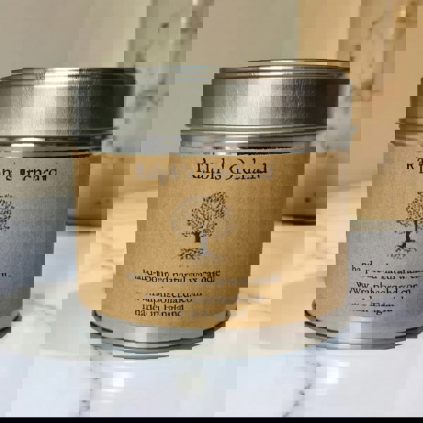 Candle in a tin labeled 'Ralph's Orchard' on a marble surface