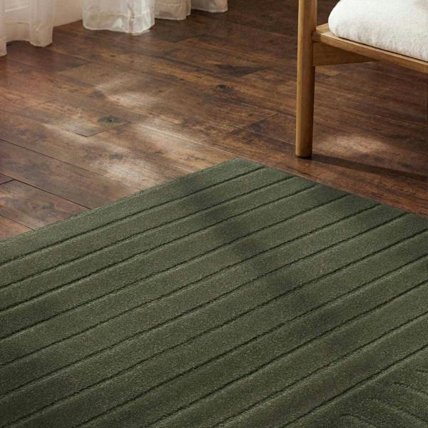 Green rug on a wooden floor with a bed partially visible