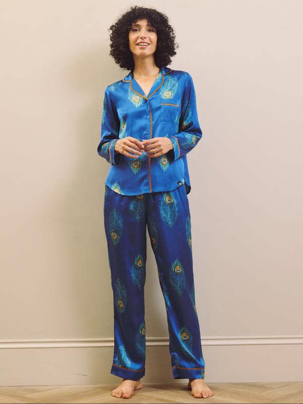 Woman wearing a blue satin pajama set with peacock feather design against a plain background