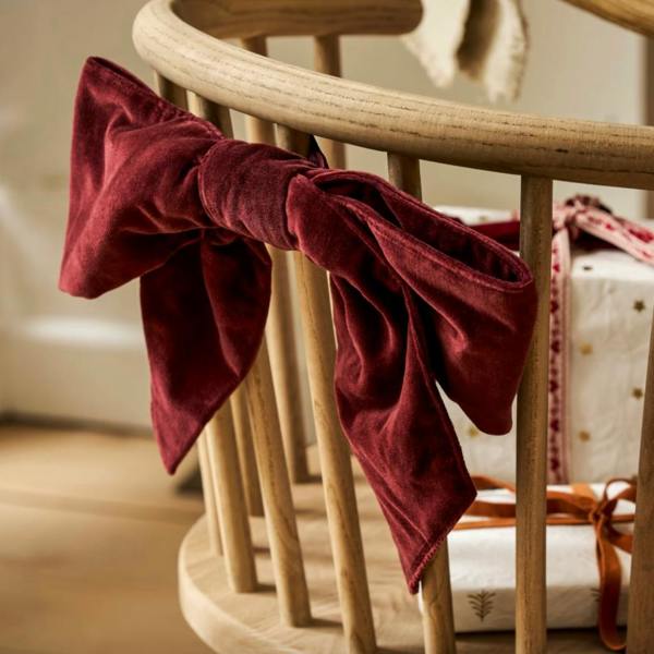 A plush berry red cotton velvet Christmas door bow tied elegantly to the wooden spindles of a chair.