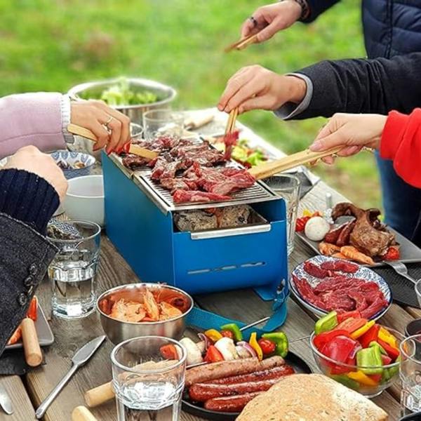 A group of friends grilling steak and sausages on a blue portable Yaki barbecue at a wooden outdoor table.