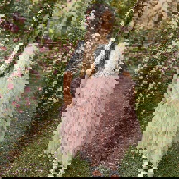 Young girl in a floral dress standing in a garden with pink flowers and a church in the background.