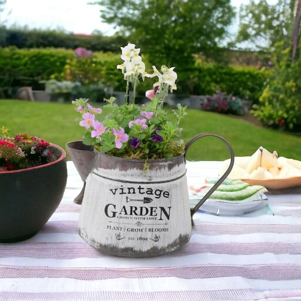 Rustic vintage jug planter filled with summer flowers including bacopa, nemesia, and calibrachoa, displayed on an outdoor garden table.