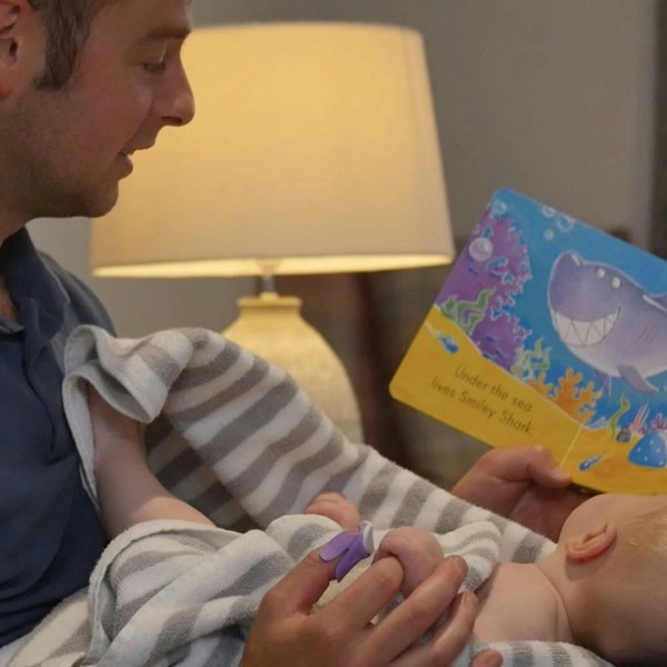 baby bonding with Daddy filing baby's nails whilst reading a book