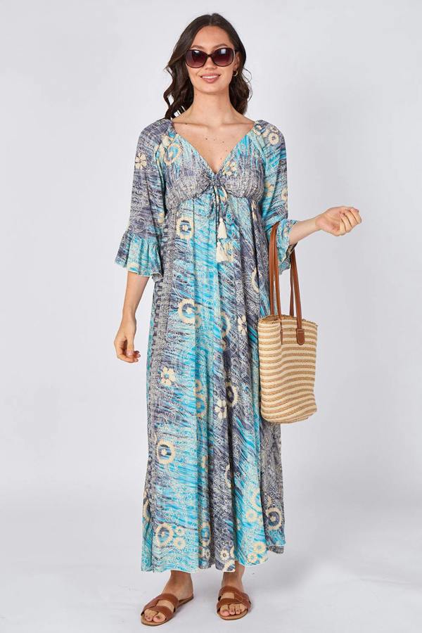Woman wearing a blue patterned dress holding a straw bag on a white background
