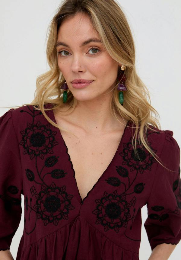 Woman wearing a burgundy dress with black floral embroidery against a white background