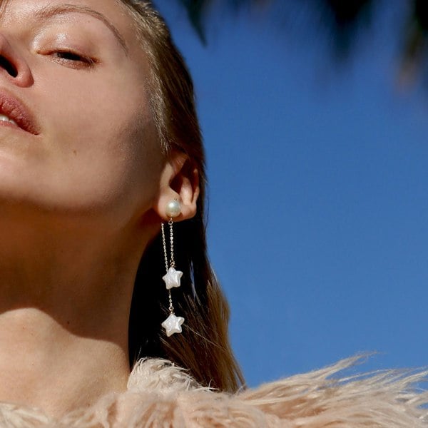 Crop of model's face with focus on star-shaped pearl earrings with blue sky behind.