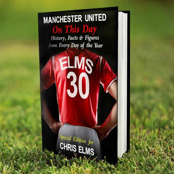 A personalised Manchester United On This Day football history hardback book standing upright on a green grass field.