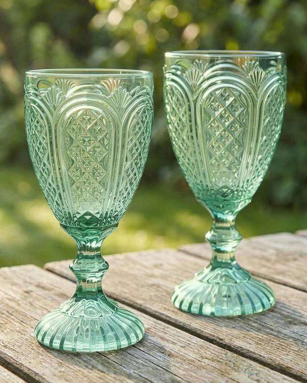 Set of green glass goblets with floral design on a wooden outdoor surface.