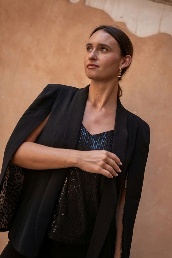 Woman wearing a black blazer over a sequin top against a beige wall