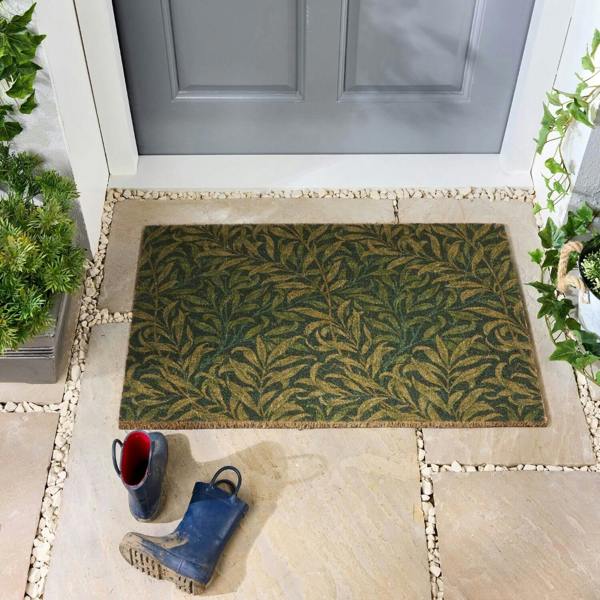 Doormat with leaf pattern on a stone patio in front of a gray door.