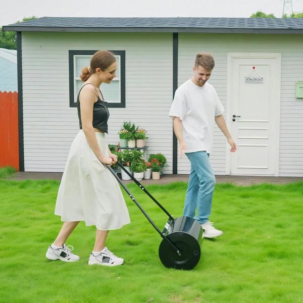 Black outdoor lawn grass roller with push handle and round drum on green turf