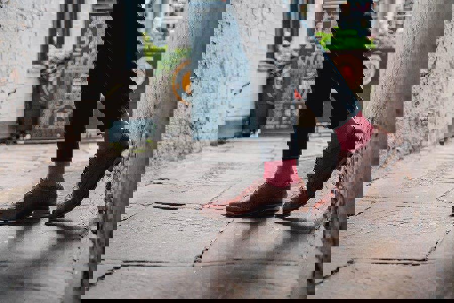 Person wearing brown shoes and red socks walking down a narrow alleyway.