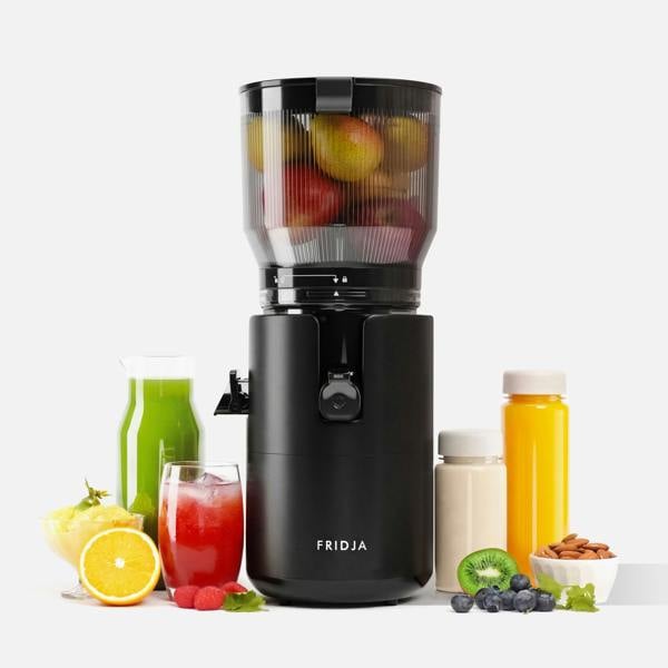 A black Fridja f2800 Open Whole Fruit Juicer filled with apples is surrounded by assorted fruits, green and red juices, jars of yellow juice and a white smoothie, blueberries, almonds, and leafy greens.